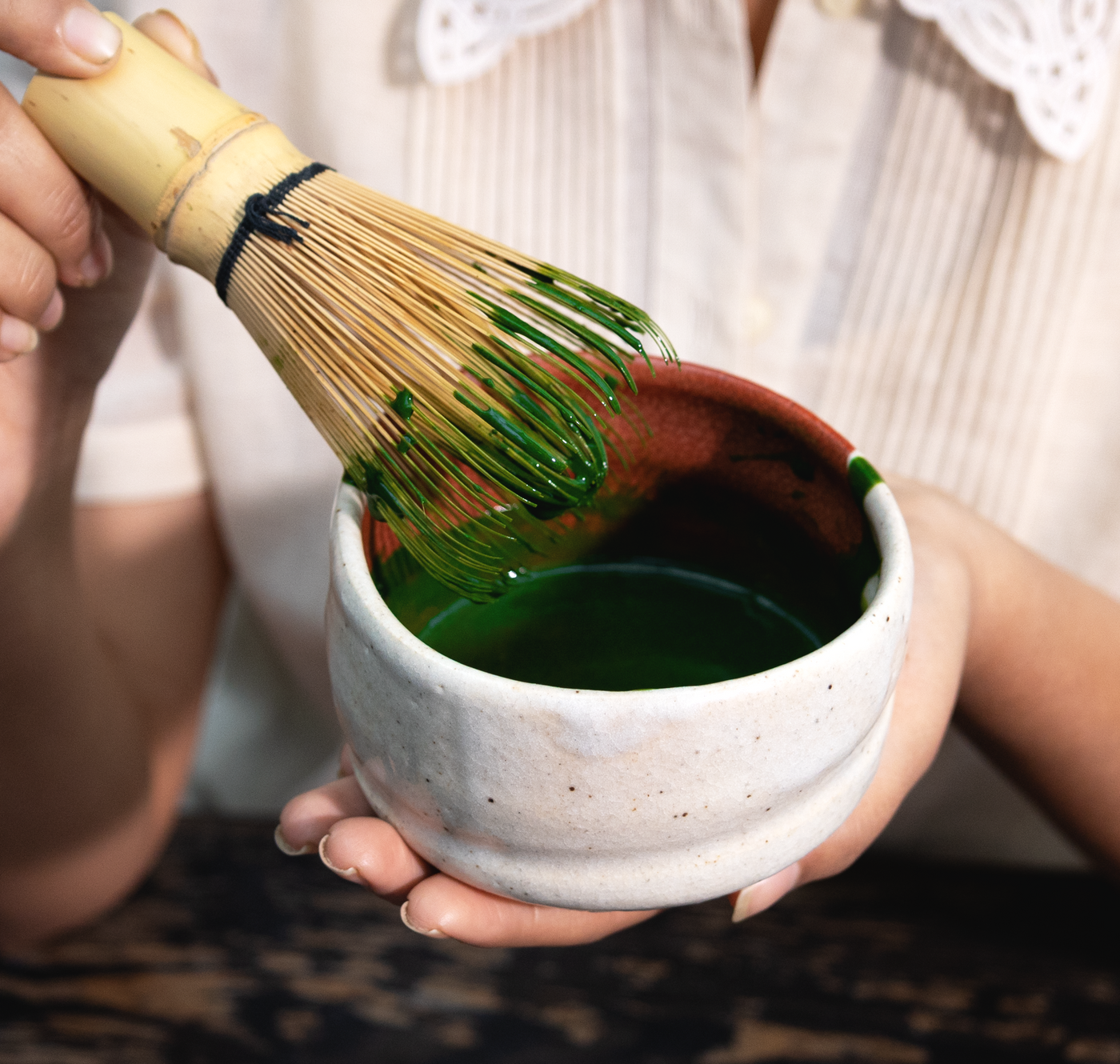 A person holding a bowl of matcha tea with a bamboo whisk.